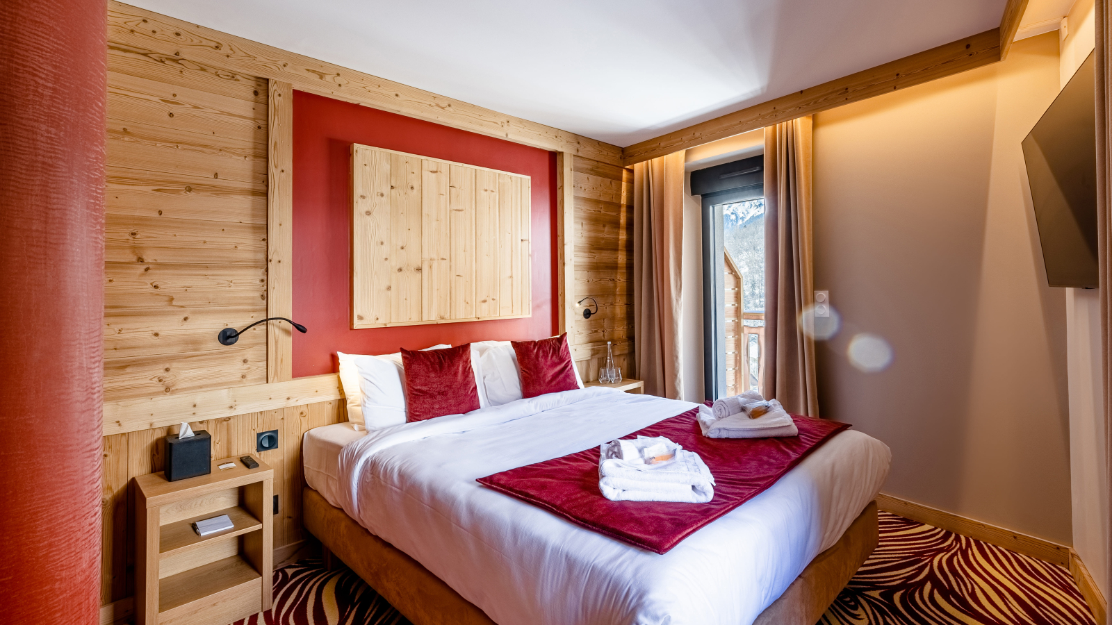 Chambre avec bois au mur et moquette rouge et beige, couvre-lit rouge velours