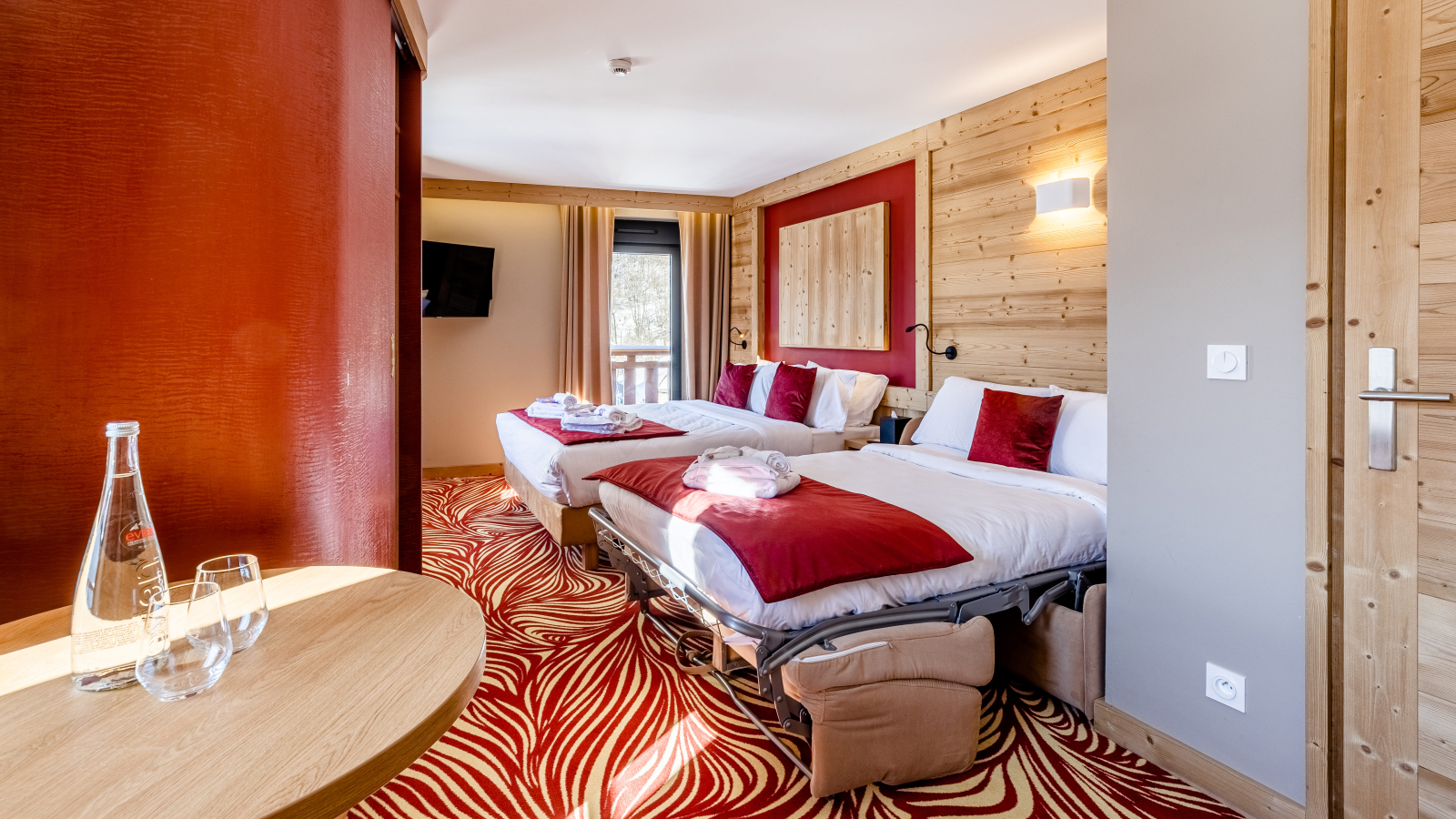 Chambre avec deux lits double et couvre lit rouge. Moquette rouge et beige et coin café.