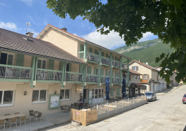 Façade avec hôtel et terrasses aux étages. Restaurant au rez-de-chaussée avec deux terrasses, parasols bleus fermés, tarifs affichés