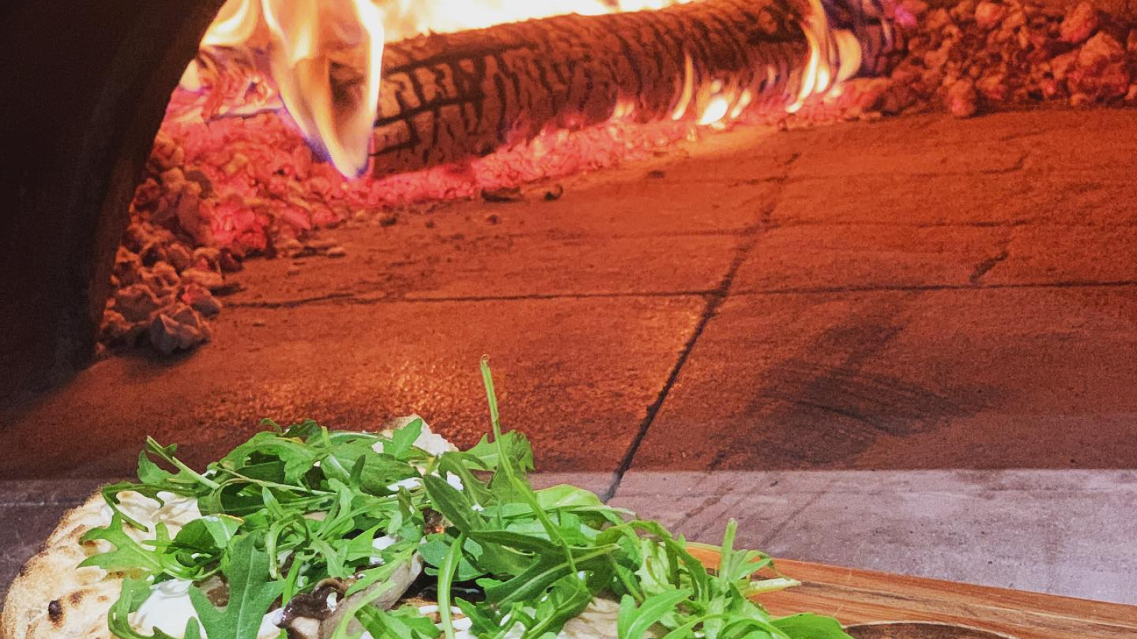 Pizza calzone avec roquettes et feu à bois en arrière plan.