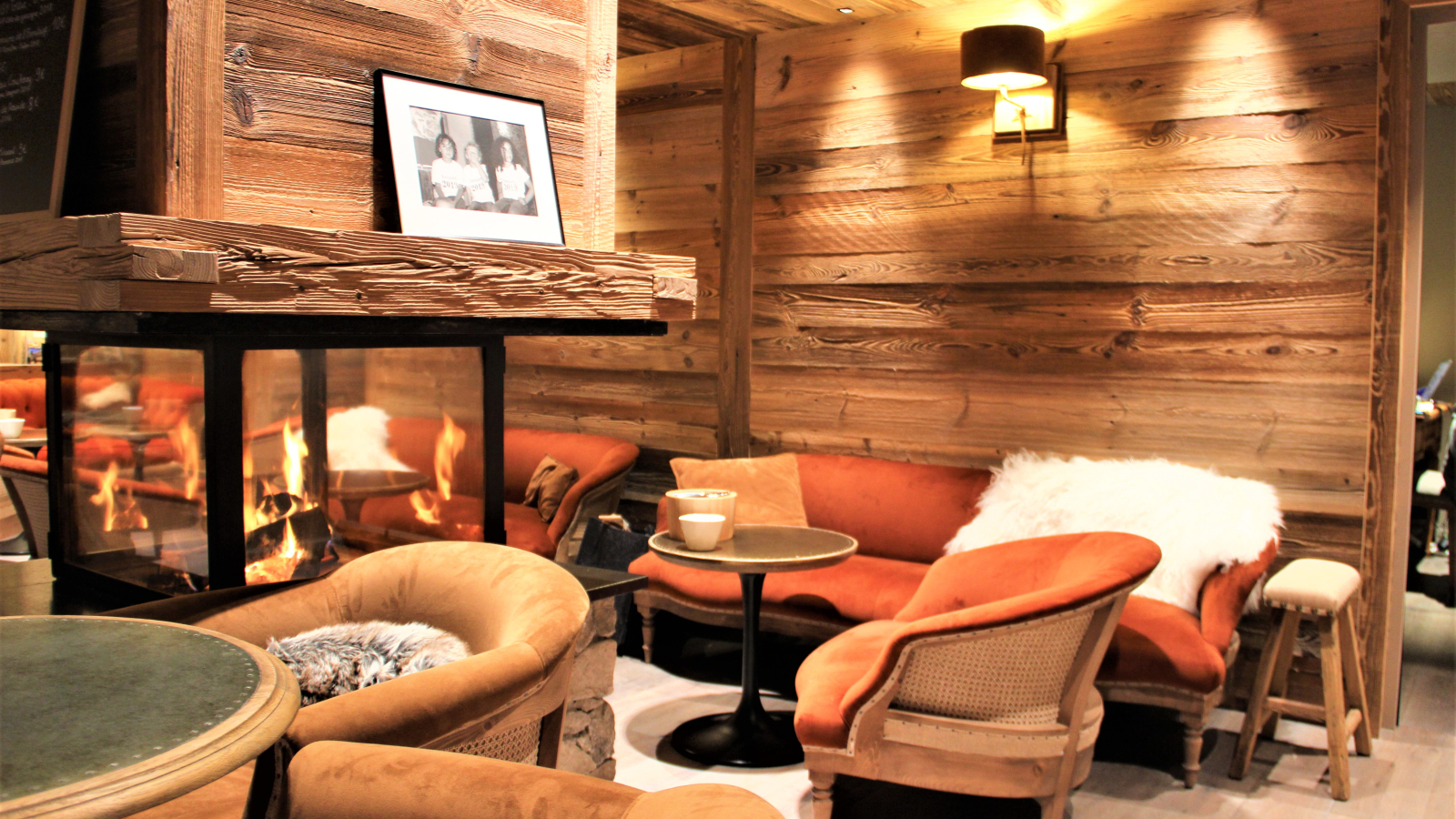 Salon ambiance chalet avec mur en bois et cheminée centrale.