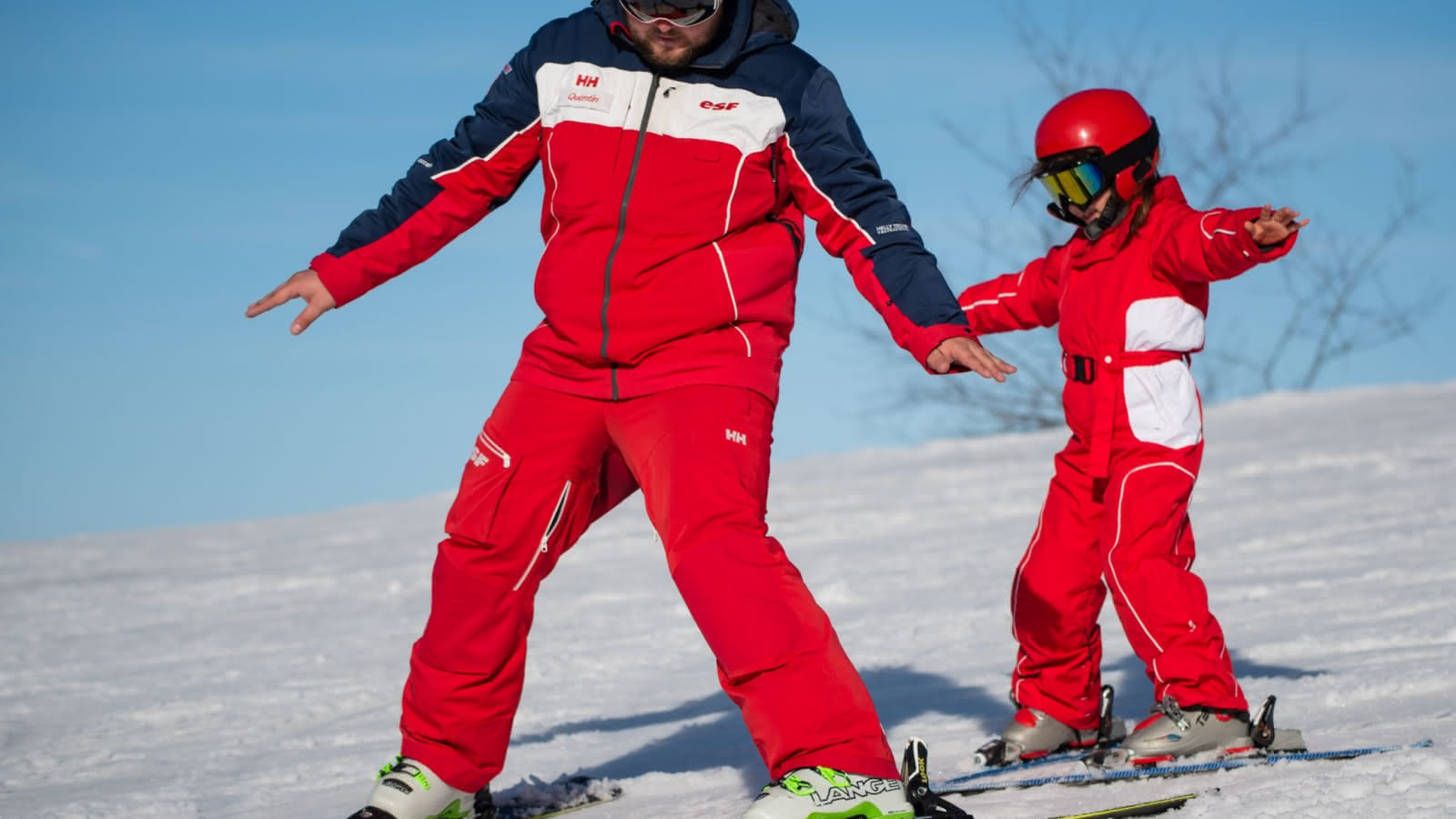 instructor and pupil on skis, red skiing suits