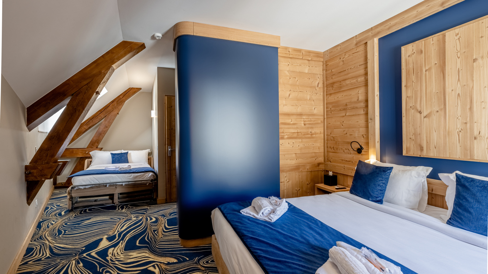 Chambre avec deux lits doubles, en soupente avec moquette bleue et beige.